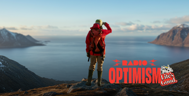A woman wearing a red hiking jacket is standing in a place where the vast ocean and snow-covered mountains can be seen. The image also features the "Radio Optimism" slogan logo and the "Life's Good." logo alongside the woman.