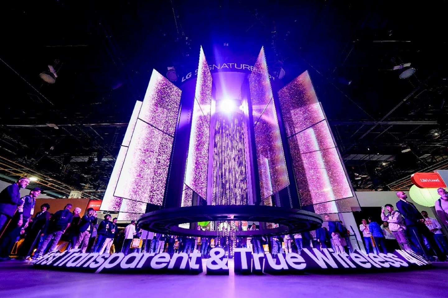 A photo of a stunning kinetic media façade made of 28 transparent slim OLED screens glowing in the dark and the people watching them