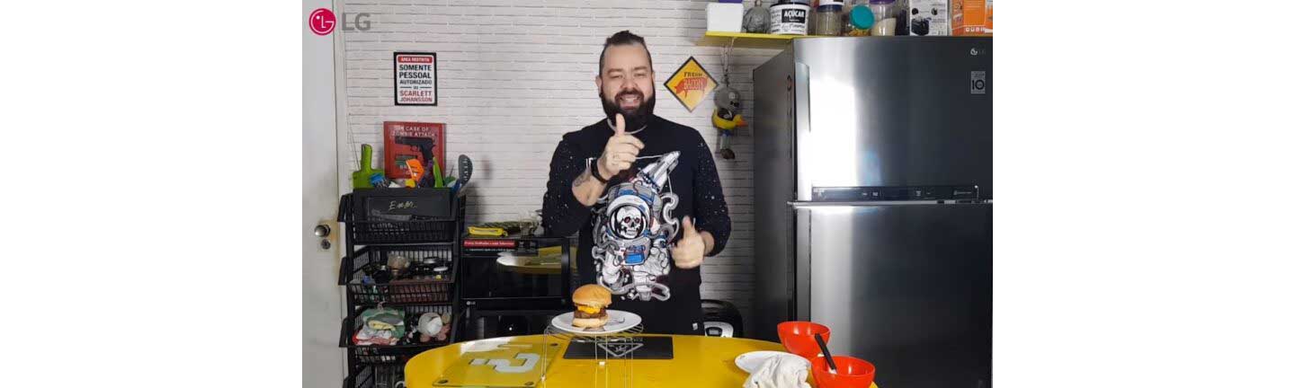 Filipe Nascimento smiles and gives a thumbs up with the burger he just made