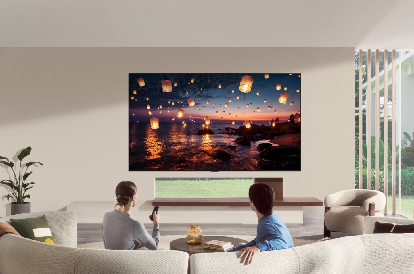 LG OLED evo AI G6 is flush-fit wall-mounted in a modern living room, displaying glowing sky lanterns at sunset while a man and woman watch from the sofa with a remote in hand.