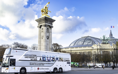 A photo of a big LG Bus with the words 'A Busan Coree' passing by the city