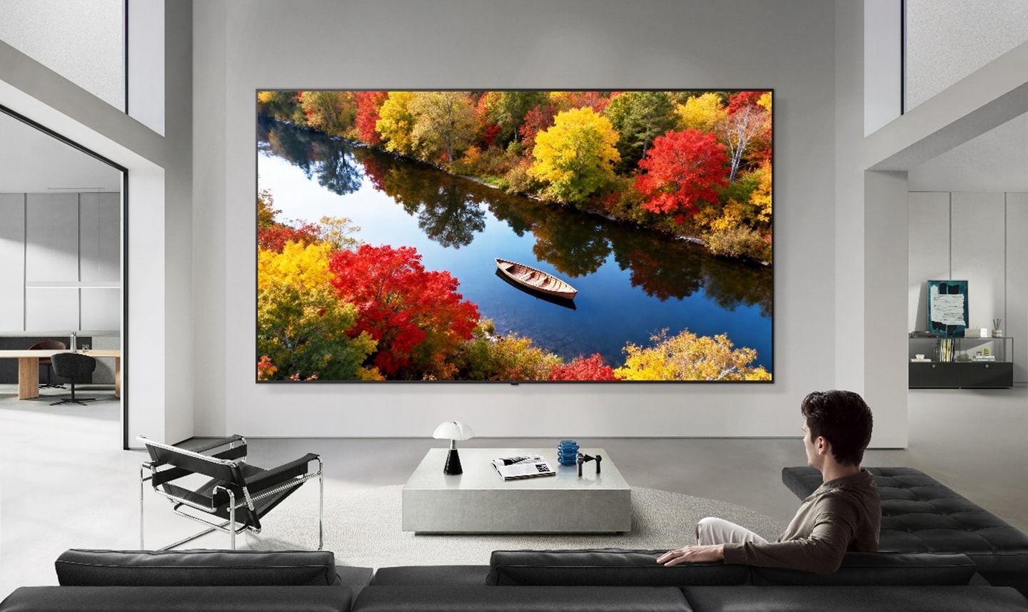 LG Micro RGB evo AI TV mounted on the wall of a modern living room is displaying a vivid autumn lake scene with a canoe in distinct, lifelike colors.
