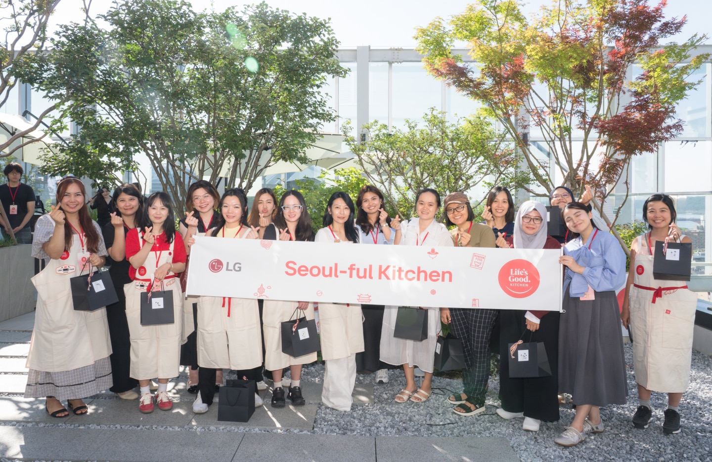A group of participants poses with a “Seoul-ful Kitchen” banner in an outdoor garden setting.