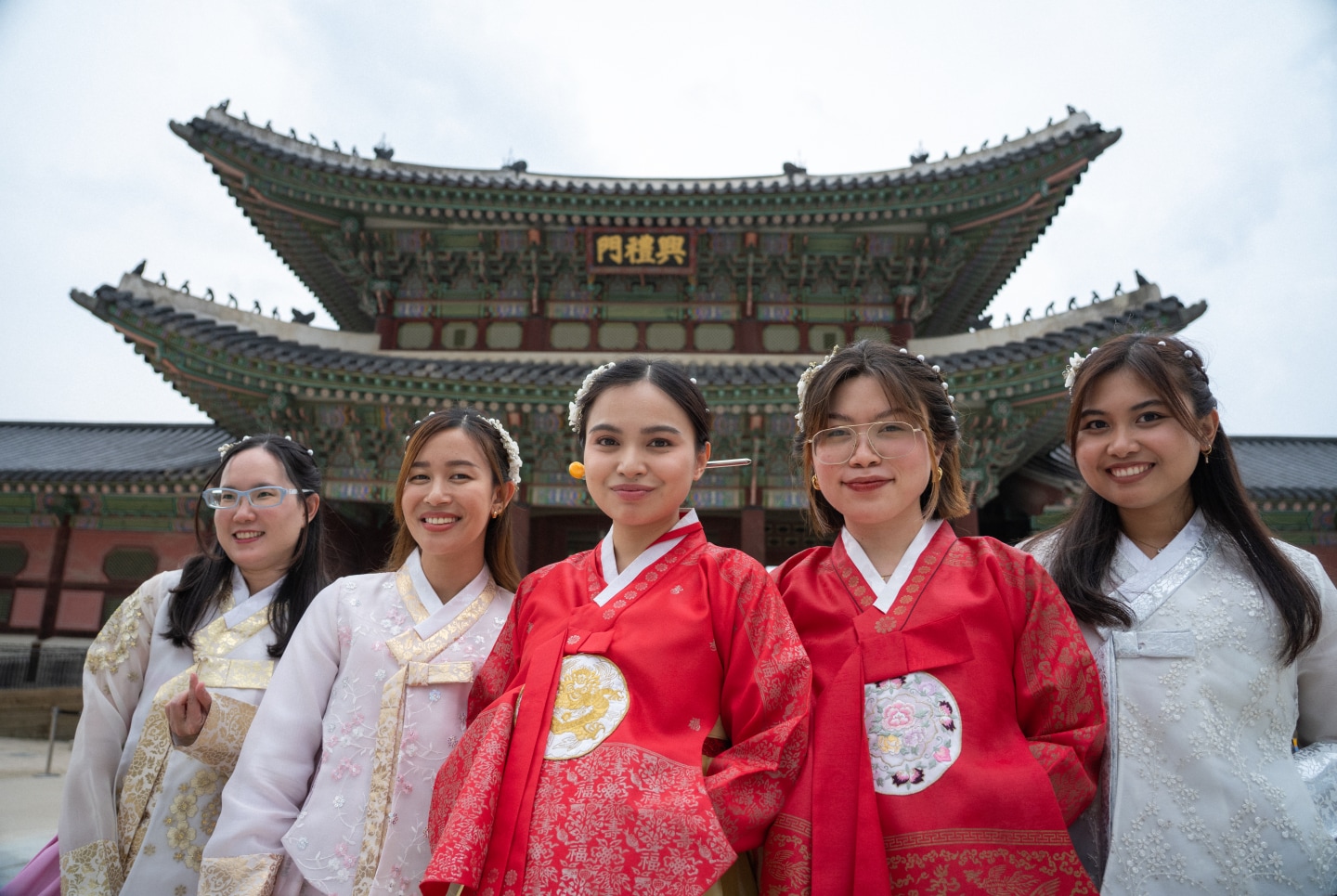 Five people wearing traditional hanbok stand in front of Gyeongbokgung Palace.