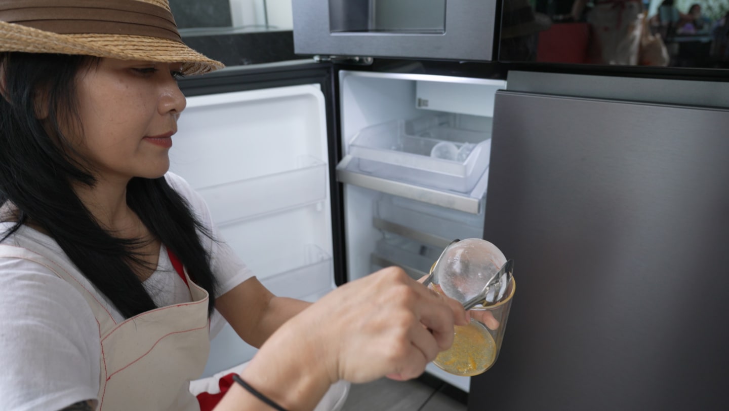 A woman wearing an apron scoops Craft Ice from an open LG InstaView™ refrigerator.