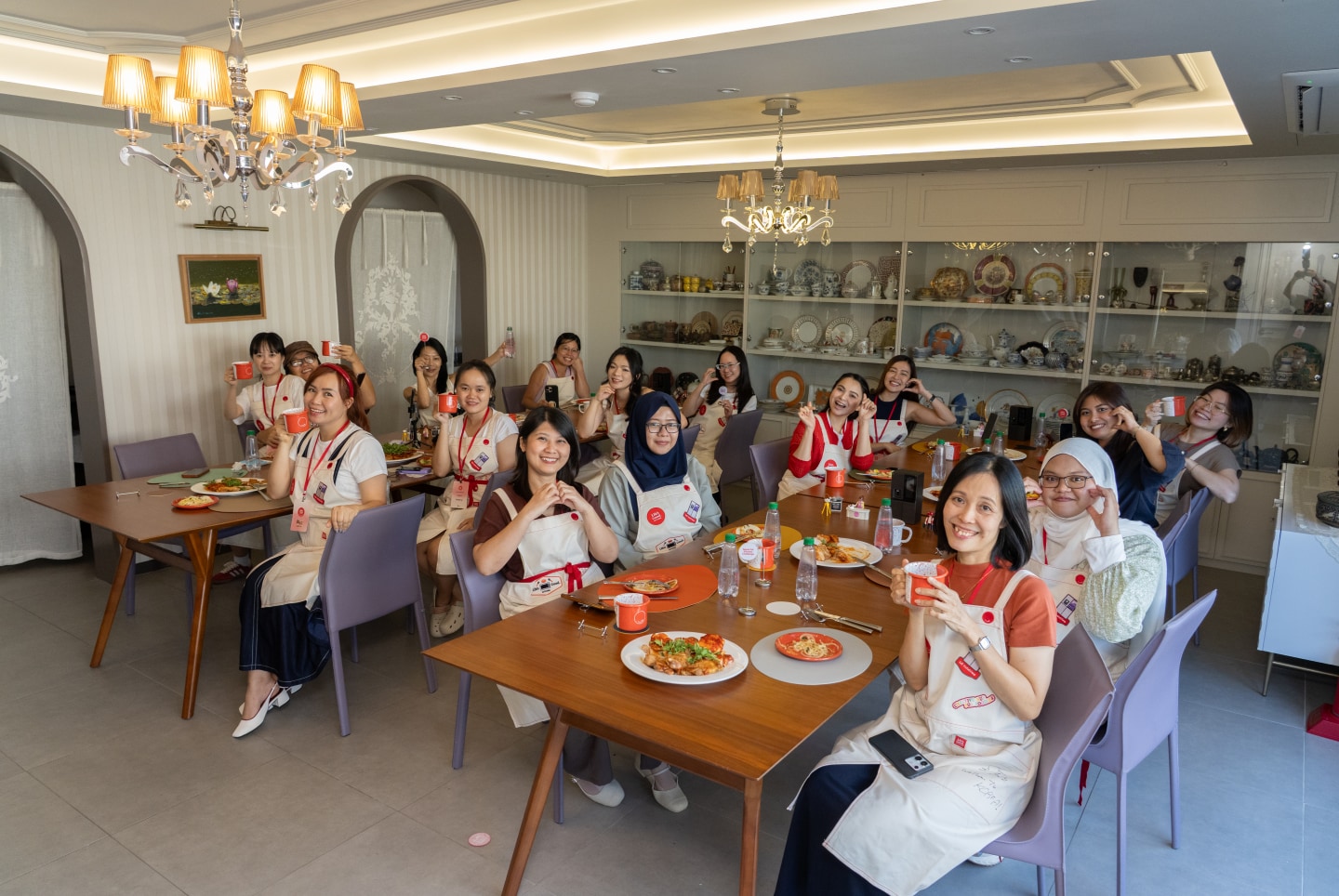 Participants sit around dining tables, making heart hand gestures and posing with their dishes during the Seoul-ful Kitchen Challenge.