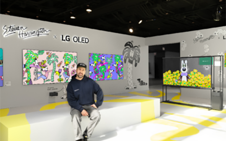 A photo of a man sitting on a couch in front of artworks in an exhibition