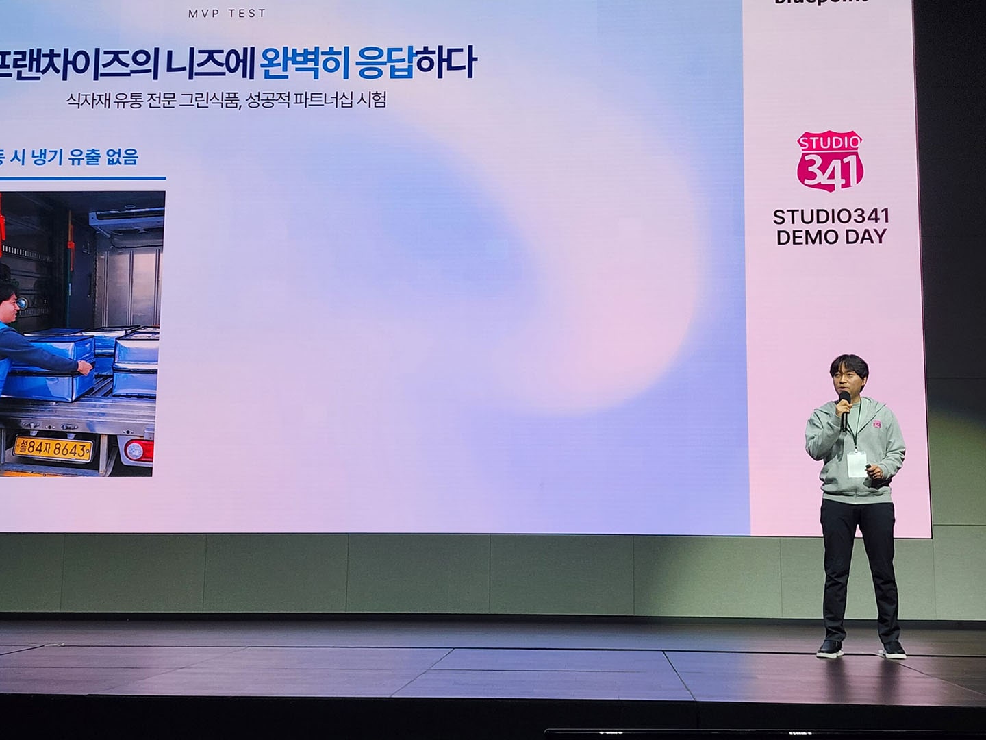 A full body shot of FRESH GO Founder Lee Sung-hoon speaking in front of a screen with a microphone 