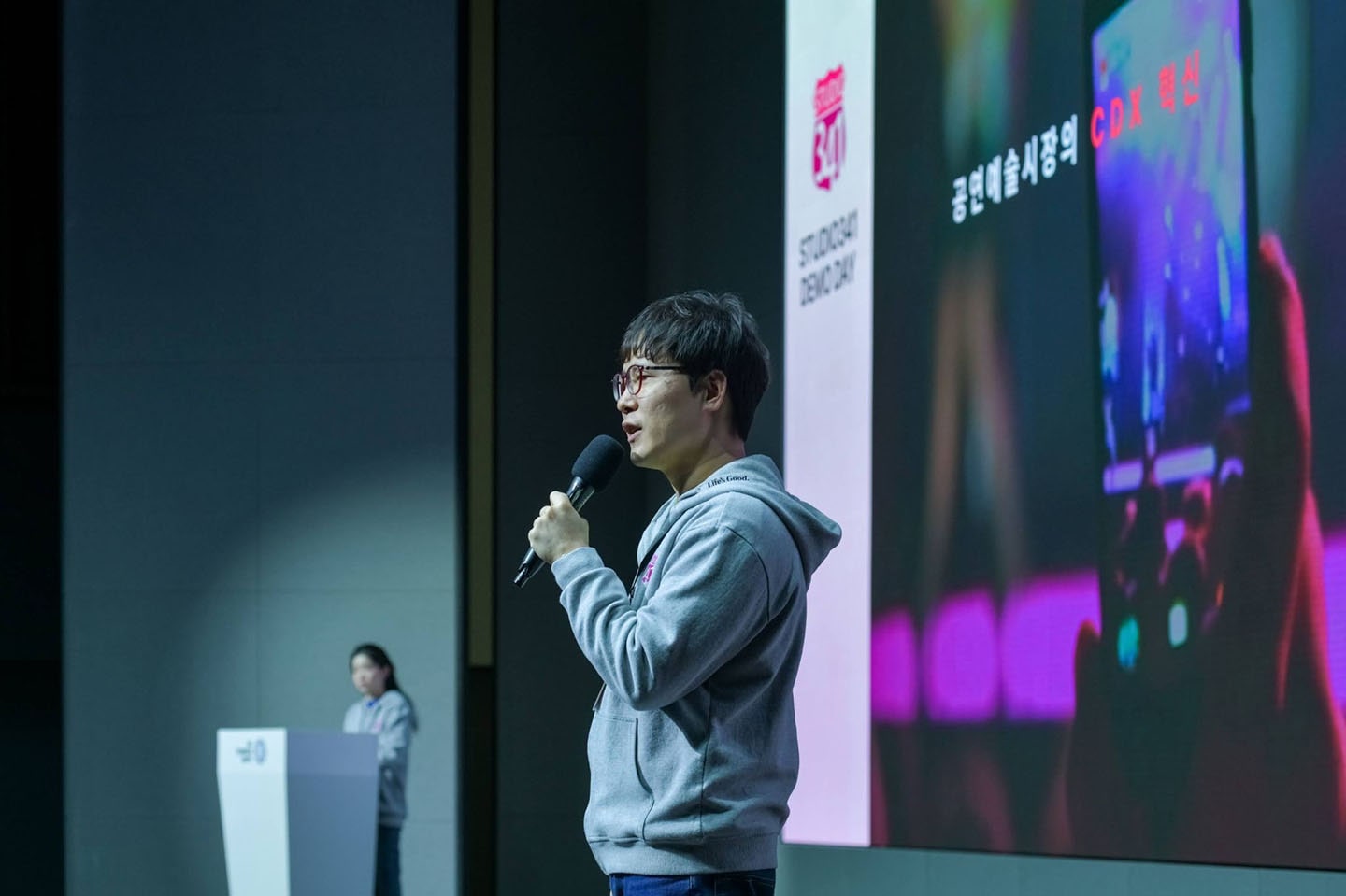 A photo of MASKIT Founder Bae Ho-yeon holding a microphone and speaking in front of a screen 