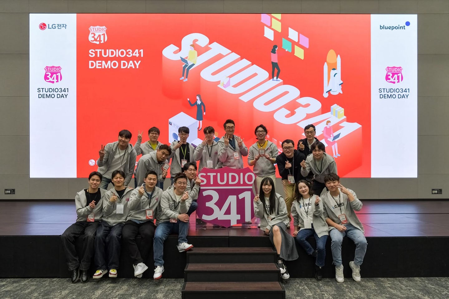 A photo of people sitting, smiling, and posing together on stage at a demo day event of STUDIO341 