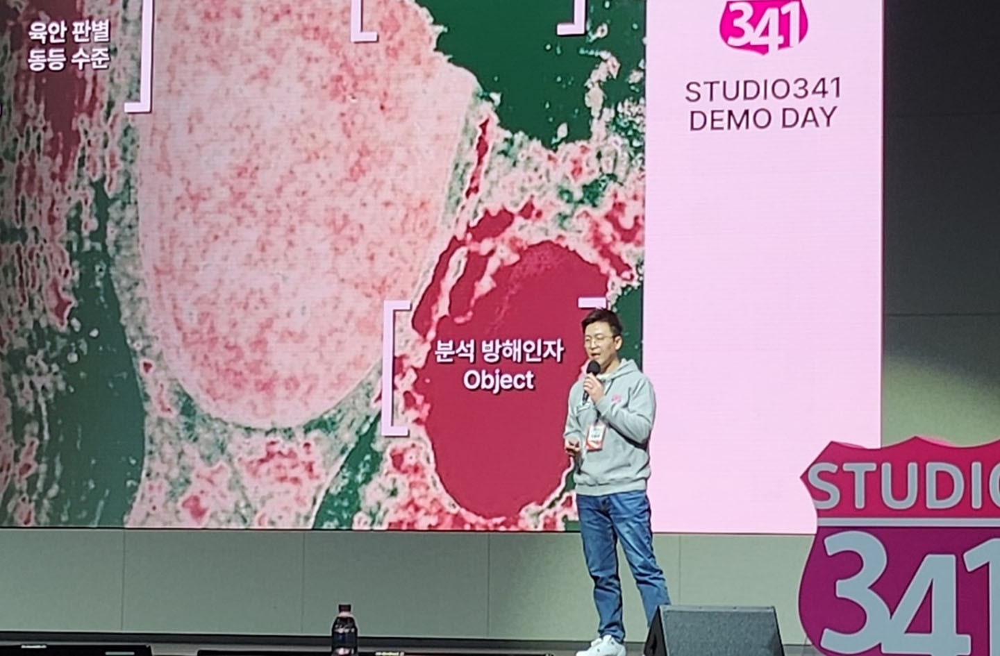 A full body shot of X UP Founder Lee Yong-soo speaking in front of a screen with a microphone