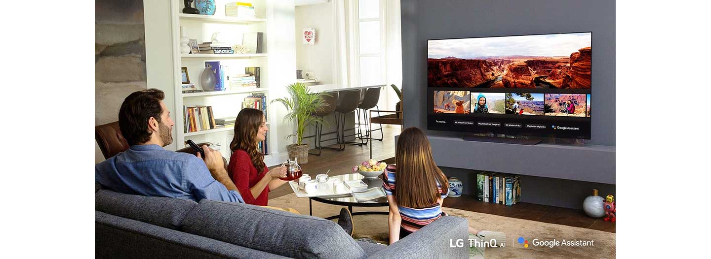 A family sits in the living room while looking at their travel photos via Google Assistant on LG’s ThinQ TV.