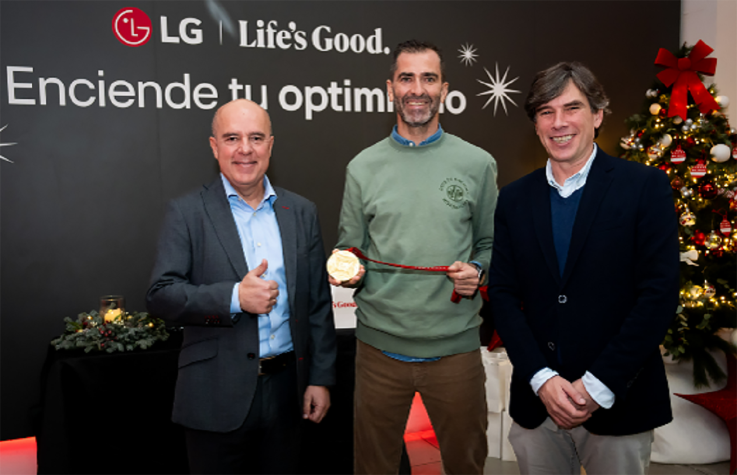 A photo of three men, including Miguel Ángel Fernández, marketing director of LG Spain, smiling and posing in front of a wall with LG's logo on it