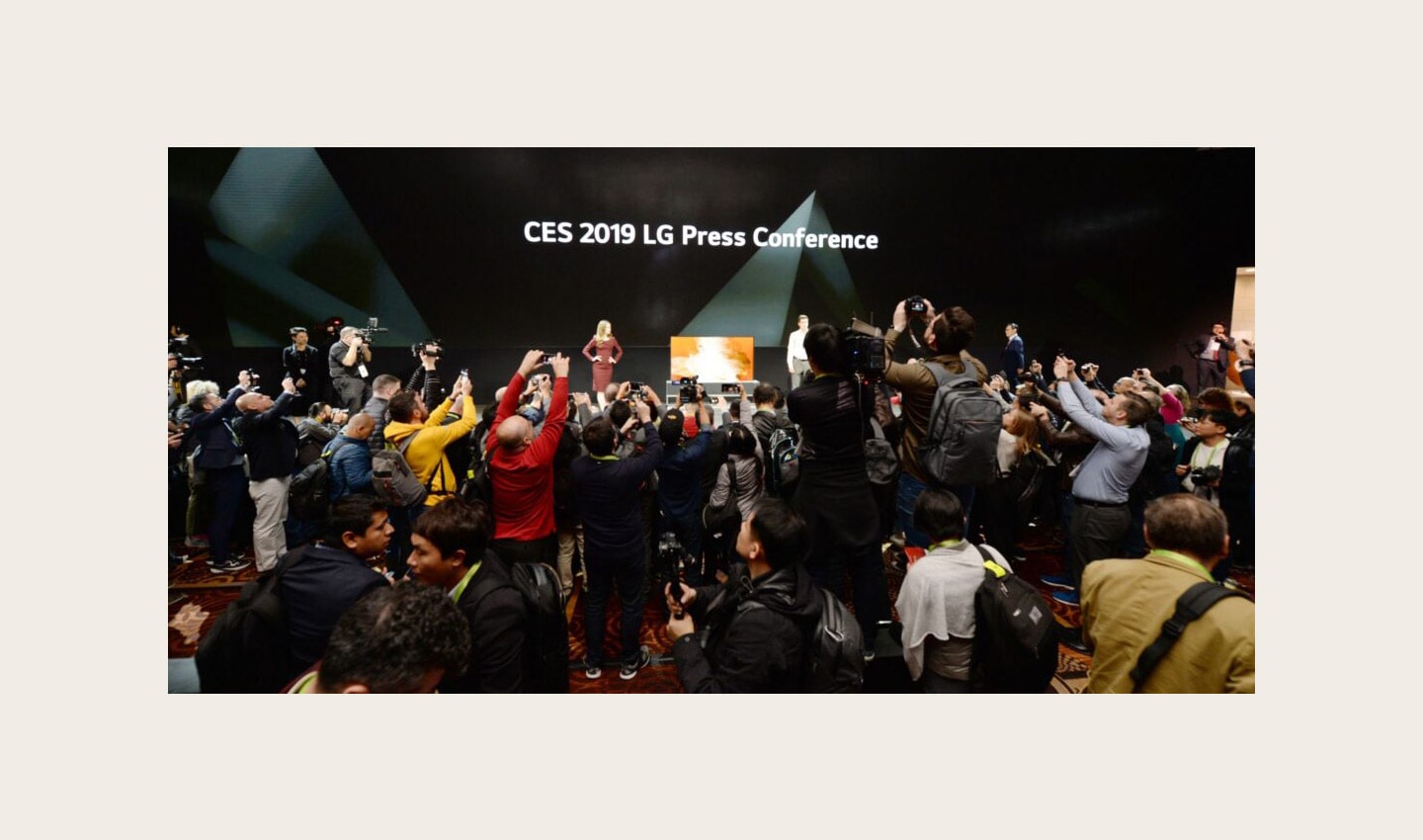 Far shot of the CES 2019 LG Press Conference with a pair of male and female models onstage posing while reporters are recording and taking pictures