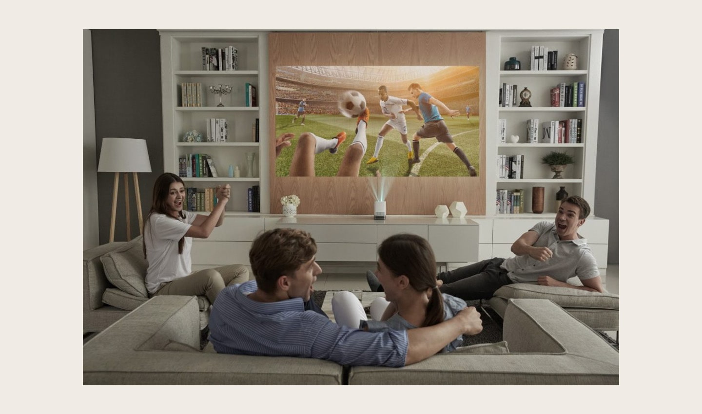 Four people sitting on couches enjoy watching a soccer game projected on the wall by the LG ProBeam Projector HF85J.