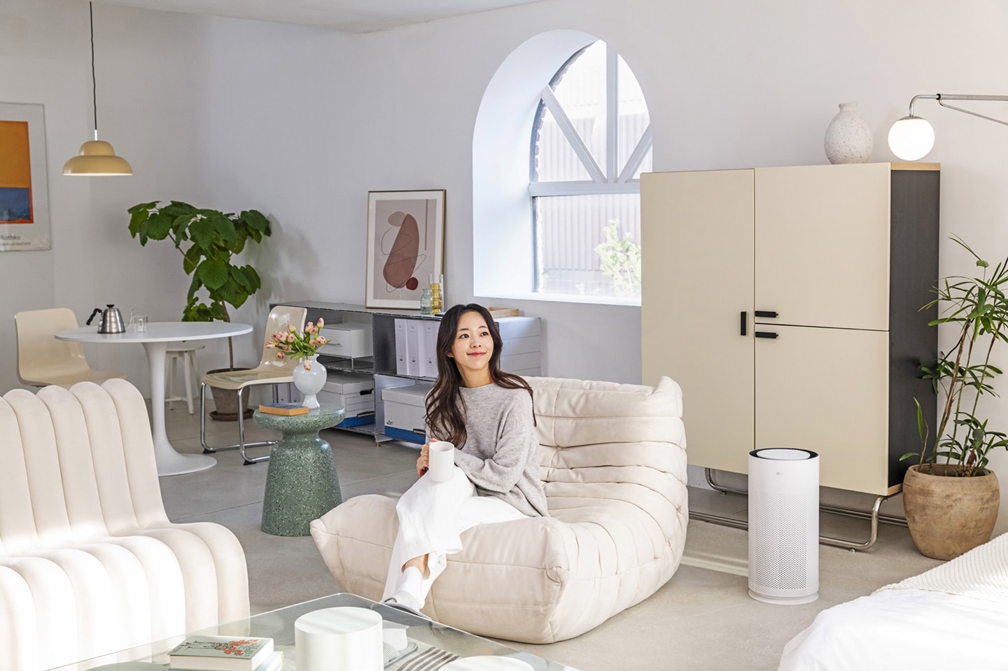 A photo of the LG PuriCare AeroHit set up in a living room besides set up in a living room beside a woman sitting on a sofa