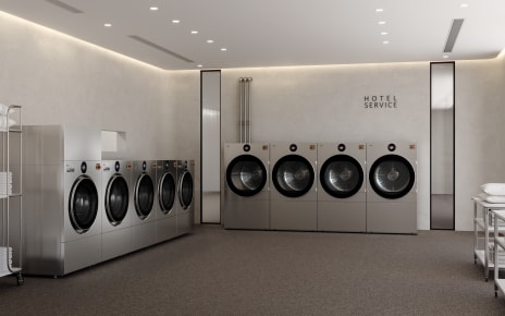 A modern hotel laundry room features, from left to right, one LG Professional WasherDryer unit, four LG Professional Washer units and four LG Professional Dryer units, with utility carts holding folded towels nearby and a “HOTEL SERVICE” sign on the wall above the dryer units.