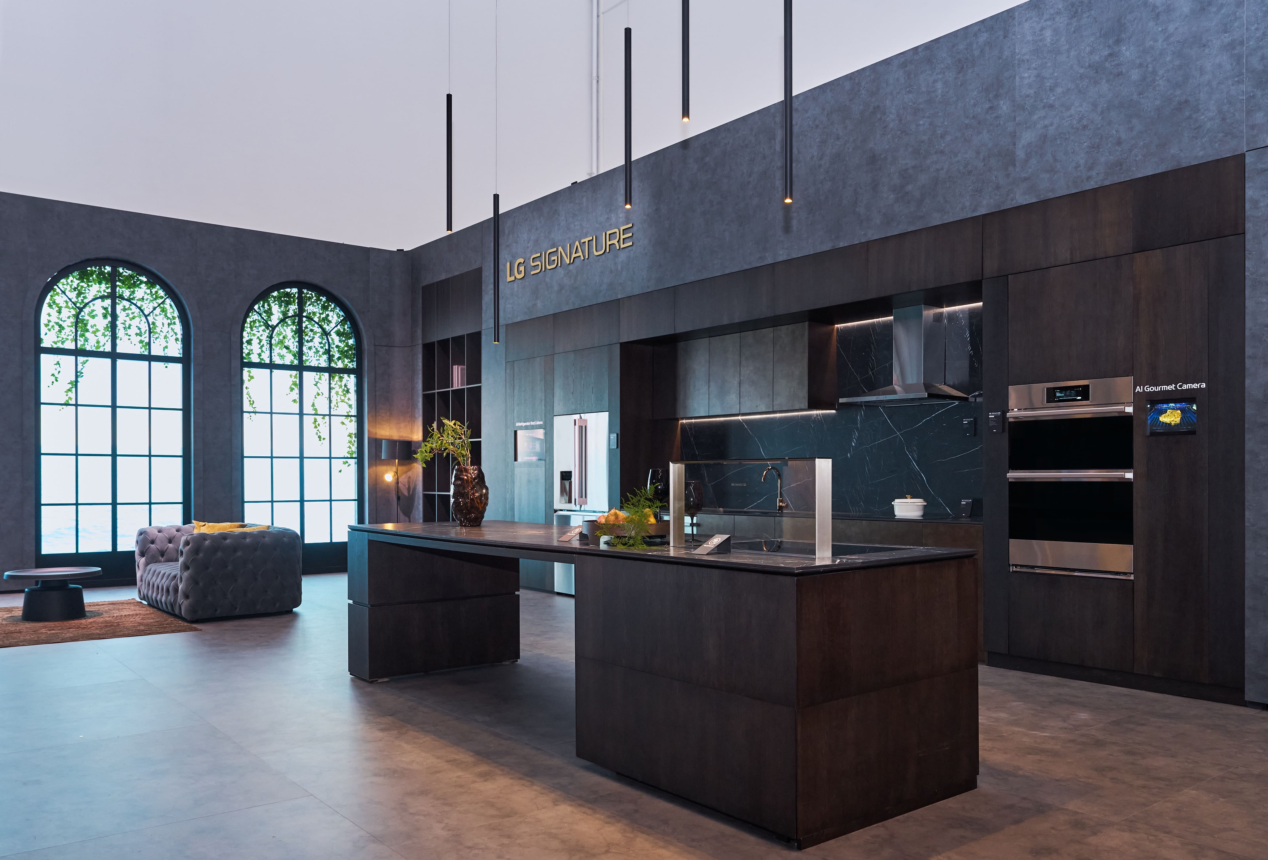 The premium LG SIGNATURE zone at IFA 2026 featuring a luxurious dark wood kitchen space equipped with an elegant island and built-in smart ovens, alongside a stylish lounge area in the background.