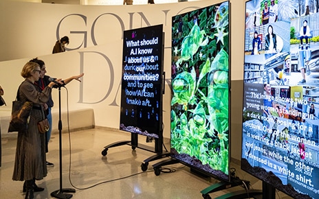 Two women are talking into a microphone as they observe Dinkins' latest works on display at ‘Late Night X Stephanie Dinkins'
