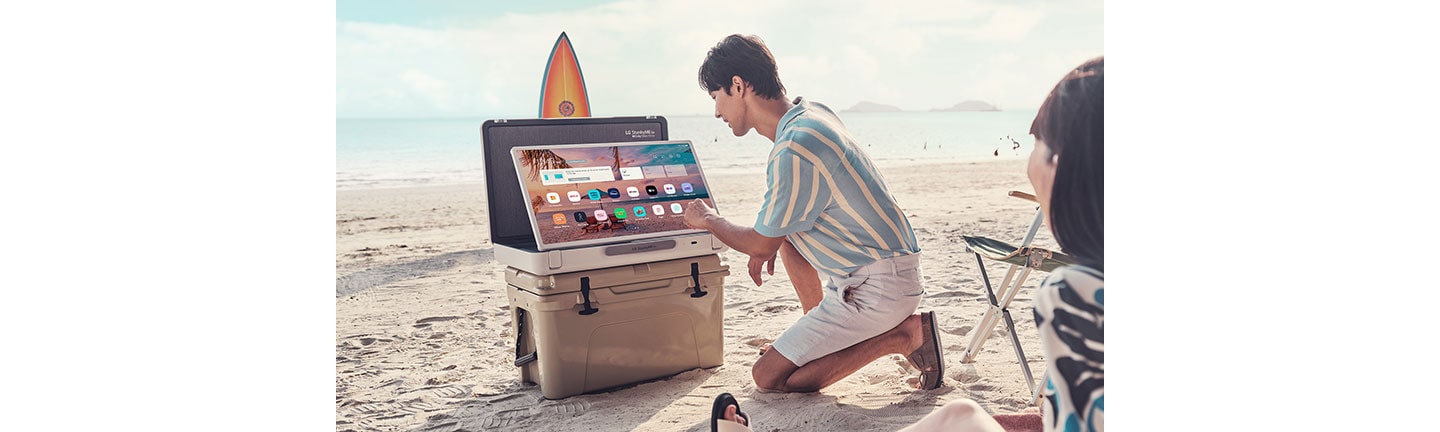 A couple using LG StanbyME Go on a sandy beach