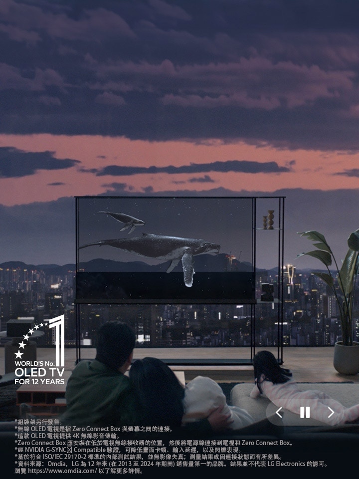 夜幕降臨，城市天際線浮現，一條鯨魚游過 LG SIGNATURE OLED T。人們坐在前景的梳化上，面向電視和窗戶。Zero Connect Box 置於電視左側的小桌子上。