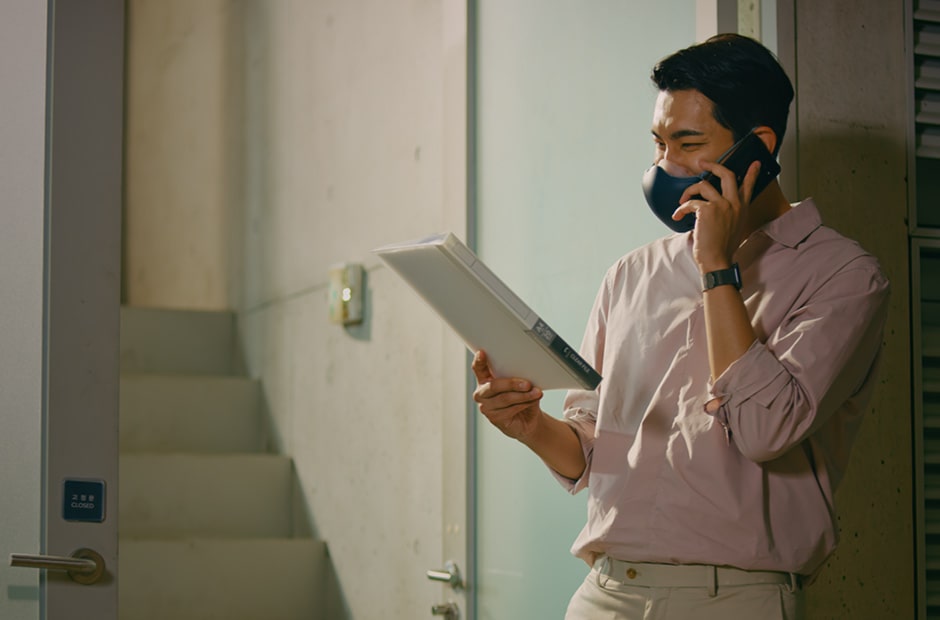 亞裔男子手持一份文件正在打電話，並配戴黑色的 LG PuriCare™ 口罩型空氣清淨機。