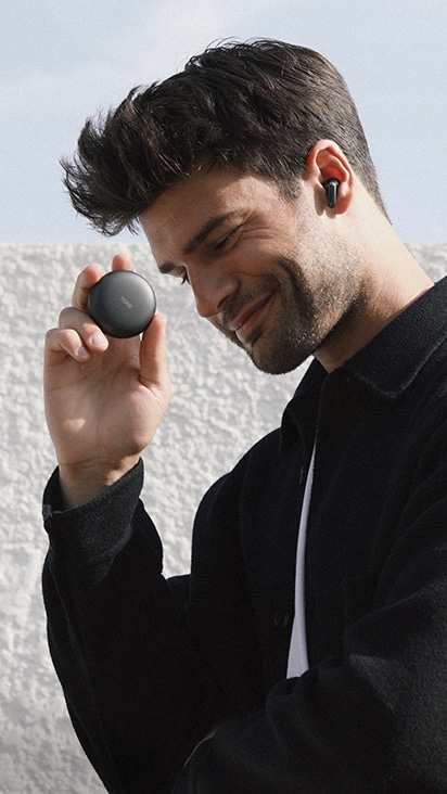 一位男士佩戴 LG TONE Free 黑色耳機、面帶微笑、手握充電盒的側視圖