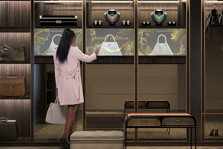 一間高檔商店的展示架上安裝了 OLED 透明顯示屏，一位女士與透明屏幕互動時，屏幕上顯示出與其後方貨架上展示的手袋完美融合的圖案。