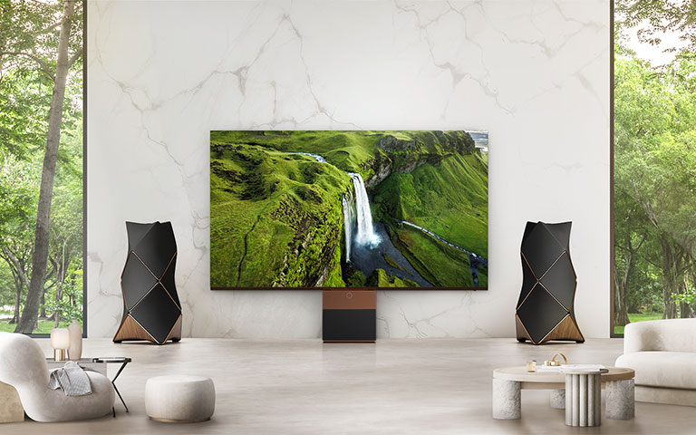 安裝在客廳牆壁上的 LG MAGNIT 生動展示了廣闊風景中的一條大瀑布，LG MAGNIT 兩側的 Beolab 90 立體聲喇叭能同時發出動態音效。