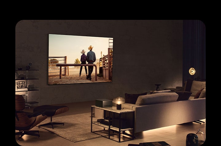 A cowboy movie plays on a wall-mounted LG OLED TV in a cozy living space in the evening. There are no wires surrounding the smart TV. The Wireless Connect Box sits neatly on a side table. The image slides out to show a different living space with a picturesque scene of a car on a highway on the LG OLED TV screen. The smart TV is on a floor stand and there are no wires surrounding it. Its Wireless Connect Box sits neatly on a side table.