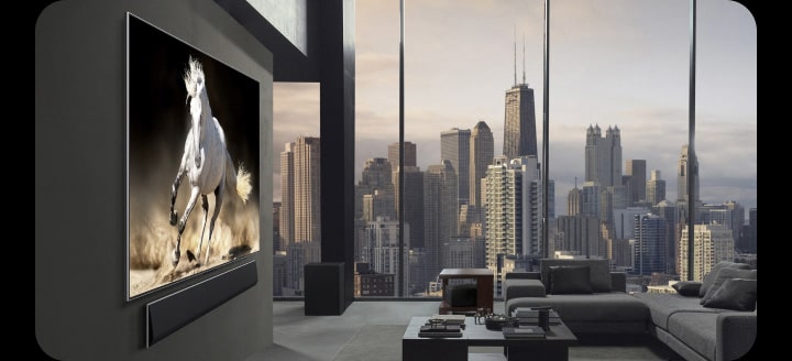 High-end penthouse apartment. City skyline is visible in the floor-to-ceiling windows of the living room. LG True Wireless TV and LG Soundbar are wall-mounted. The design of the space is very sophisticated and tidy. Zero Connect Box can be hardly seen under one of the side tables.