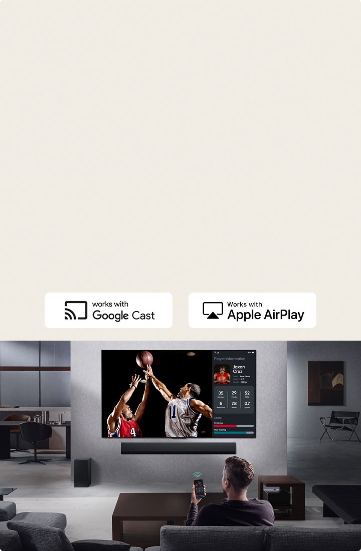 Person in their living room holding their phone. On the phone is a transmitting icon showing that the phone screen is being mirrored on the TV. On the TV is a basketball game to the side is the mirrored screen, showing player statistics. 	