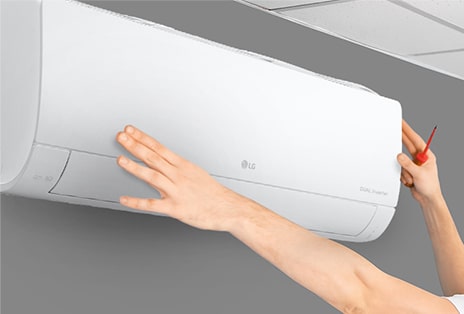 The side view of the air conditioner can be seen on the wall. Two hands are reaching up, one holding a tool, showing the ease of installation.