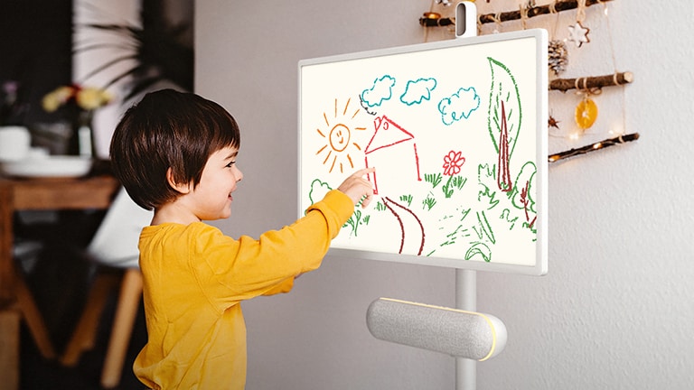 The LG StanbyME is placed in the kitchen with the LG StanbyME Speaker XT7S attached. A child draws on the screen, and the speaker's yellow mood lighting is on.