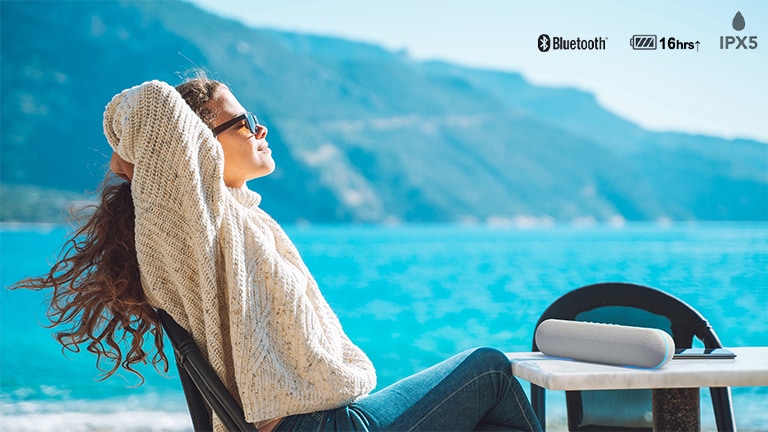 A woman enjoying music on the outdoor terrace with LG XT7S speaker.