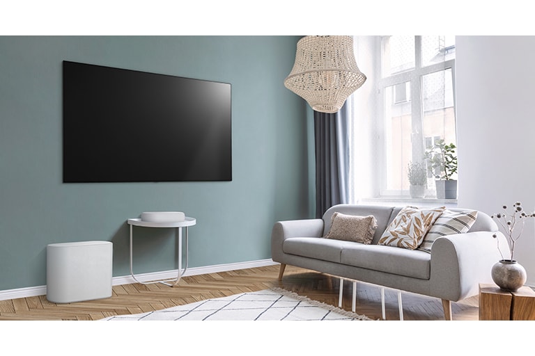 A soundbar is placed on a small tea table,  a subwoofer placed on the left side and TV is placed above a soundbar. The room is overall white.