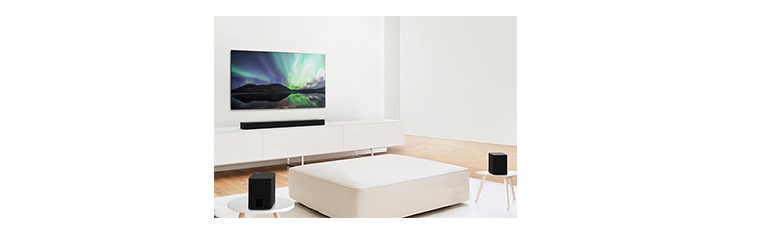 TV and sound bar in white living room with white sofa in the center. Speakers sit on both ends of the sofa.
