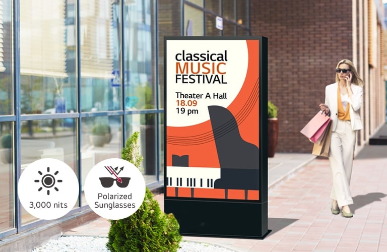 A large-sized display is installed on the street, and a woman is looking at a vivid-quality advertisement on the screen.