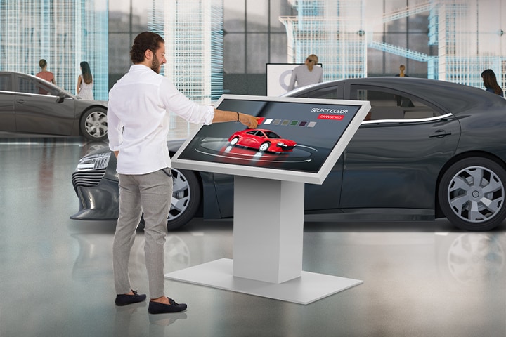 In a car dealership, a man is touching TNF5P to change the color of a car on the display.
