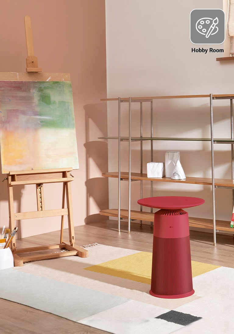 Hobby room with an easel, painting, shelves, and a red LG air purifier side table on a multi-colored rug.