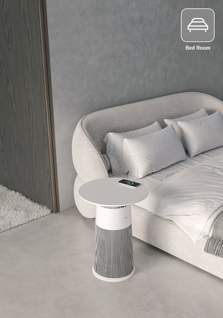 A cozy bedroom with a white sofa bed, pillows, and an LG air purifier table charging a smartphone, next to a wooden door.