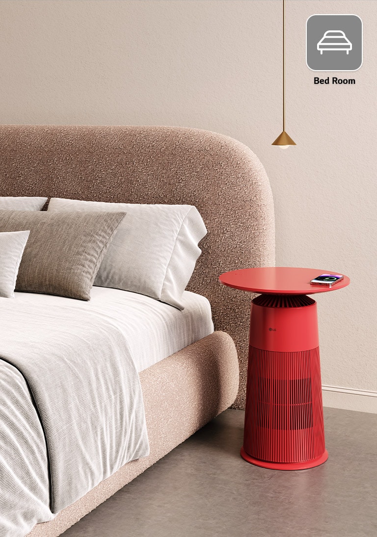 Beige bed with grey pillows, a red LG side table holding a phone beside it, and a gold pendant light above.