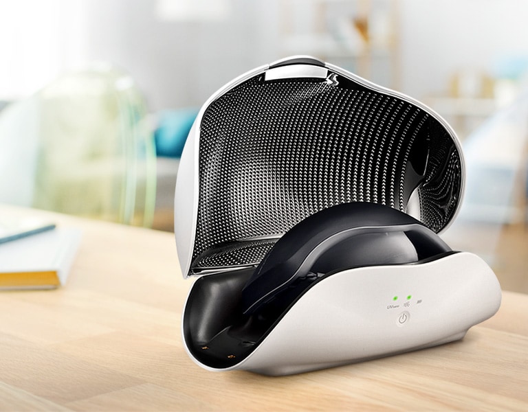 LG UV LED mask sanitiser in white and black, open on a wooden table in a modern, softly lit room with blurred background.