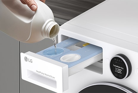 LG white front load washer dryer has its detergent drawer open, showing a close-up of a hand pouring liquid detergent inside.