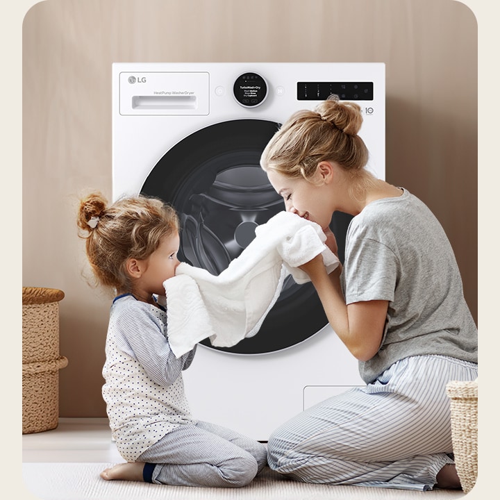 LG white front load washer dryer is in front of a mother and baby smelling a clean white towel together.