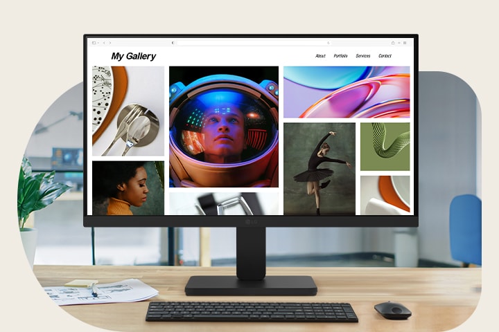 A modern desktop workspace featuring an LG monitor displaying a vibrant photo portfolio. The monitor is centered on a clean wooden desk with a keyboard, mouse, coffee cup, headphones, and potted plant. In the background, a man works near a large window in a contemporary office setting.