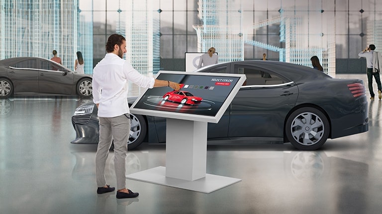 In a car dealership, a man is touching TNF5J to change the color of a car on the display.