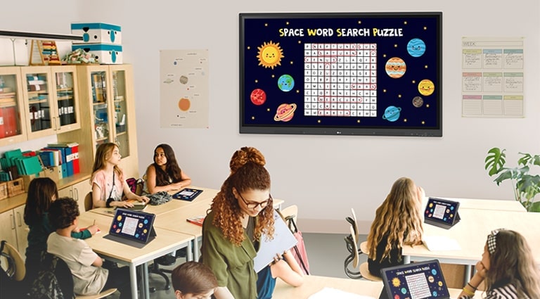 A aula está sendo ministrada em sala de aula, e a tela do material da aula que fica exposta no quadro digital TR3DK da parede da sala de aula está sendo compartilhada nos tablets dos alunos.