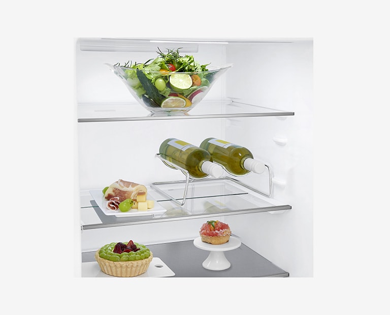 Fresh salad on top shelf, wine bottles on middle shelf, pastries, cheese, and grapes on bottom shelf inside a refrigerator.