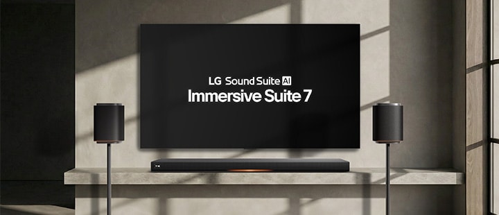 A Sound Suite M7 speaker set is placed on stands in front of a TV mounted on a gray-toned wall and a Sound Suite H7 is placed below the TV.